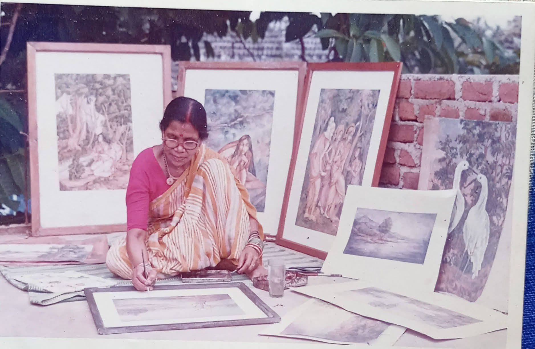 Basanta Kumari Samanta seated outdoors painting, surrounded by her framed watercolour works