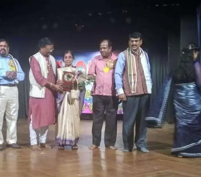 Basanta Kumari Samanta being presented a plaque on stage by a group of dignitaries